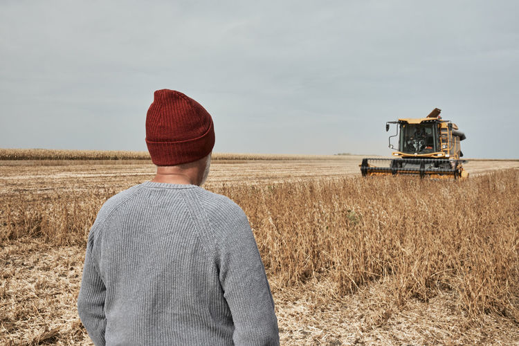 Farmer looking at tractor harvesting crop while standing at farm