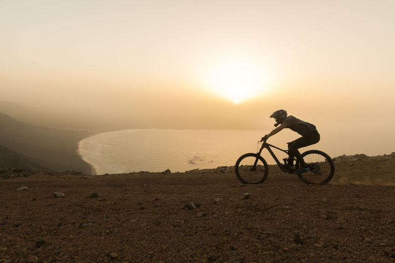 Spain, lanzarote, mountainbiker on a trip at the coast at sunset