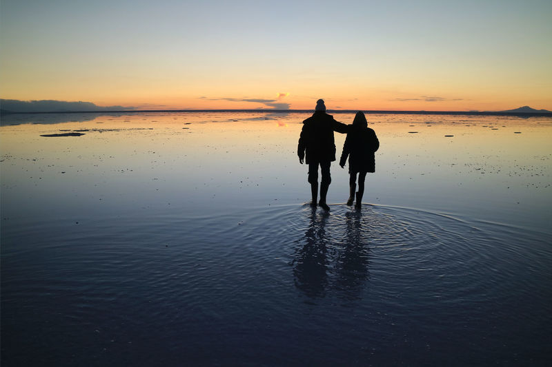 Silhouette couple on beach against sky during sunset