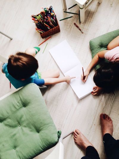 Low section of parent with kids sitting on hardwood floor at home