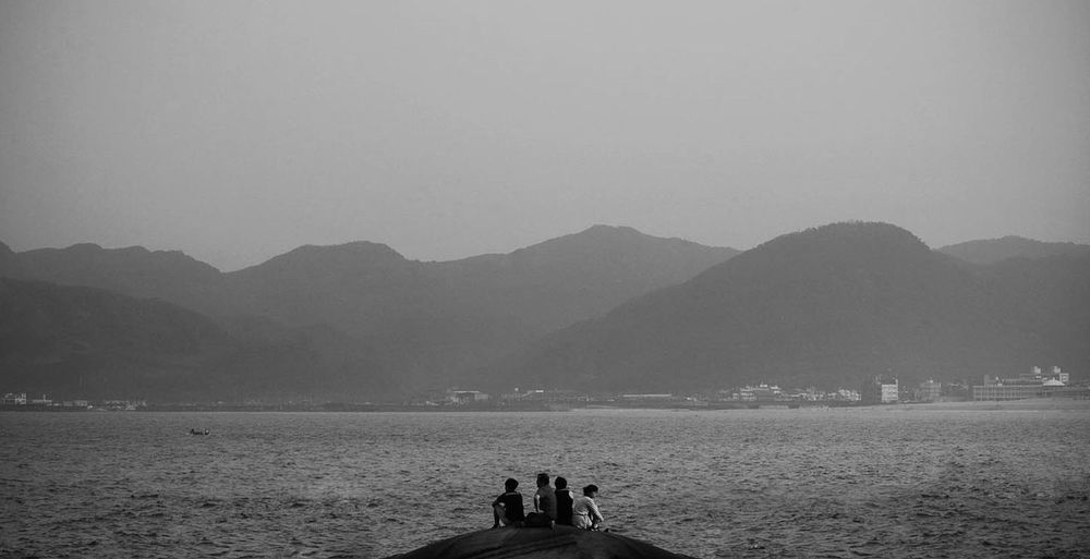Friends sitting by sea against mountains