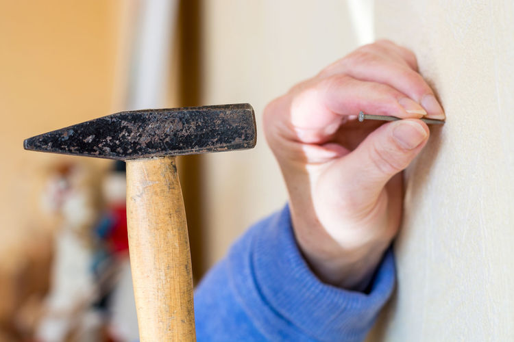 Cropped hand hammering nail on white wall