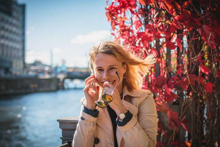 Portrait of cheerful young woman talking on phone by river