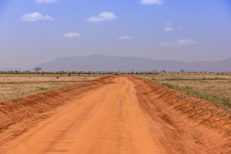 Dirt road amidst field against sky