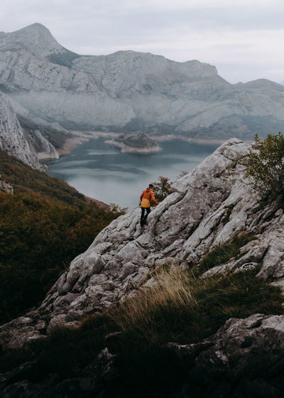 Man climbing on rock by mountains and lake