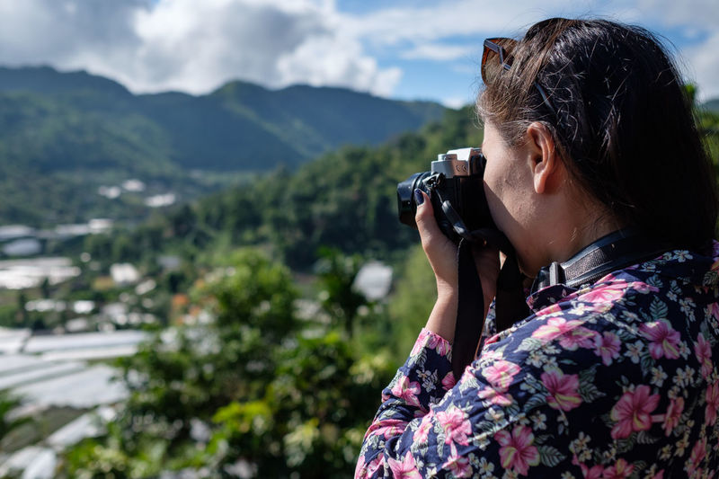 Side view of woman photographing with digital camera on mountain
