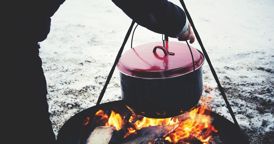 Cropped image of man heating cooking utensil outdoors during winter