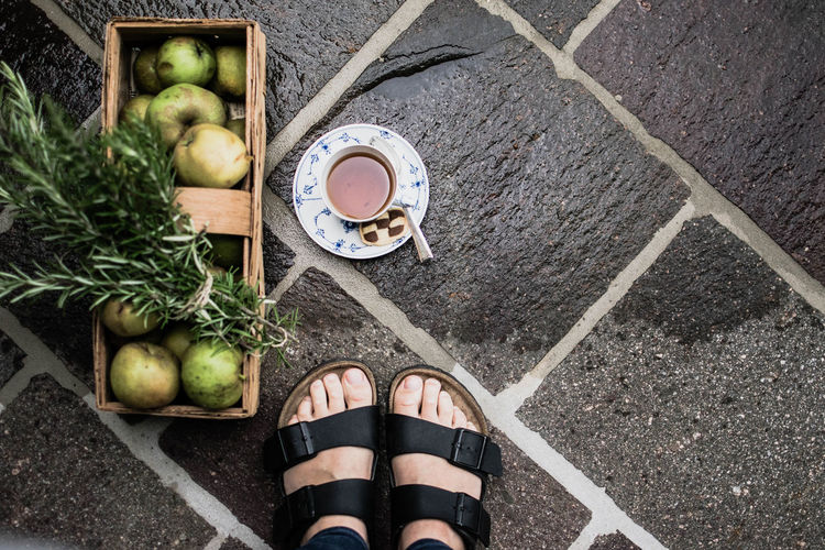 Low section of person standing by apples in container and tea cup on wet footpath