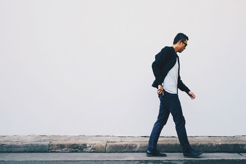 Young man walking on street against white wall