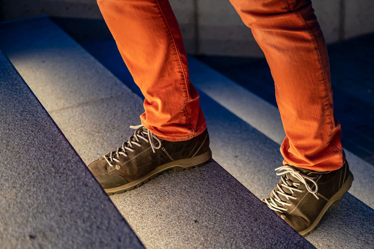 Male legs in walking boots and red jeans climb the illuminated stone steps on a winter evening