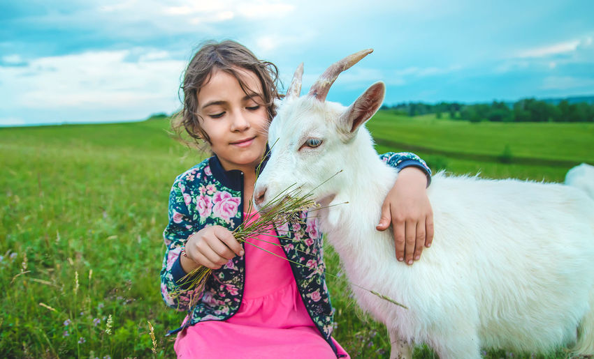 Girl feeding grass to goat in meadow