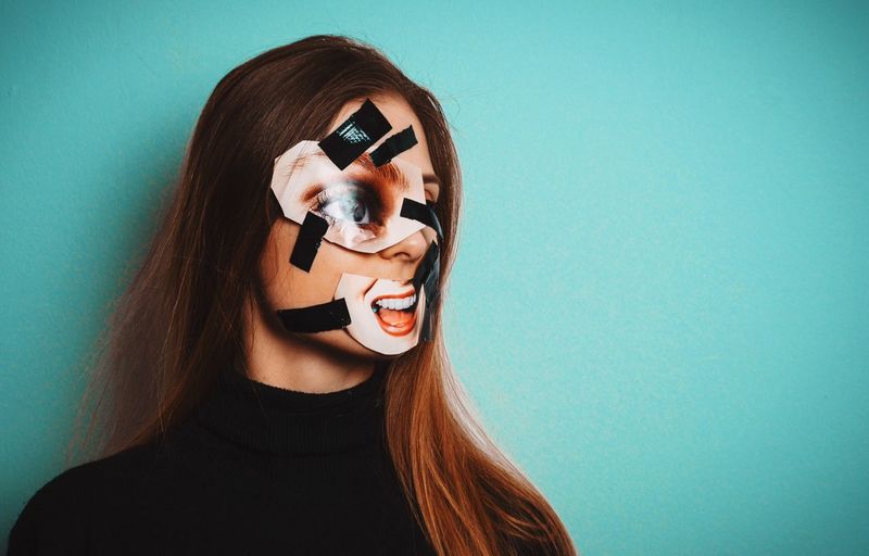 Woman with duct tape and photographs on face against wall