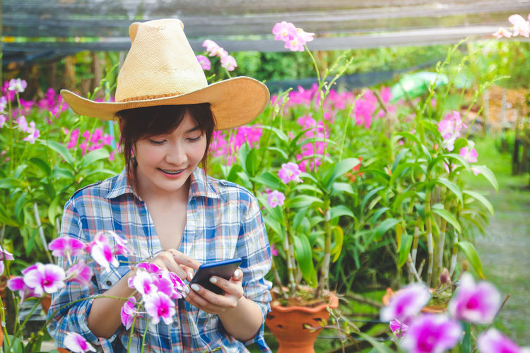 Young woman using mobile phone while standing against plants