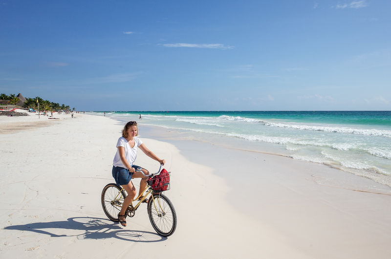 Woman riding horse on beach against sky
