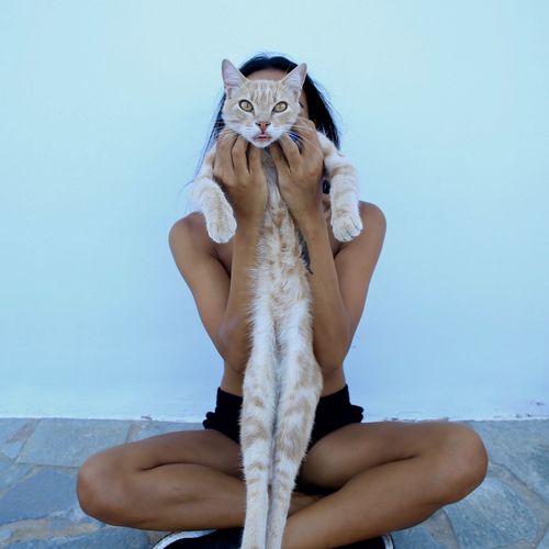 Portrait of young woman with cat against white wall