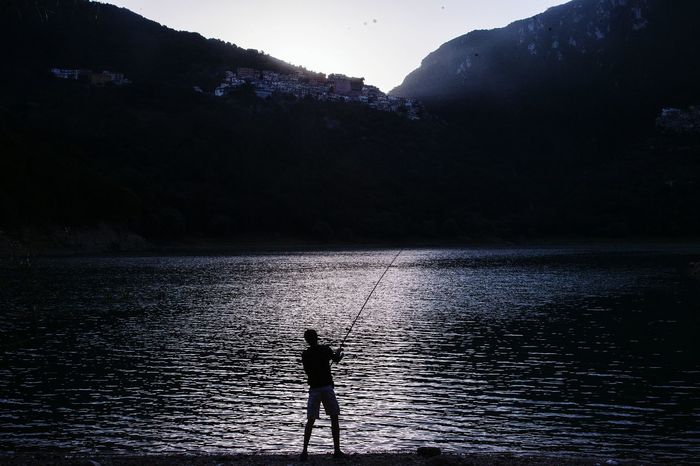 Rear view of silhouette man fishing at lakeshore