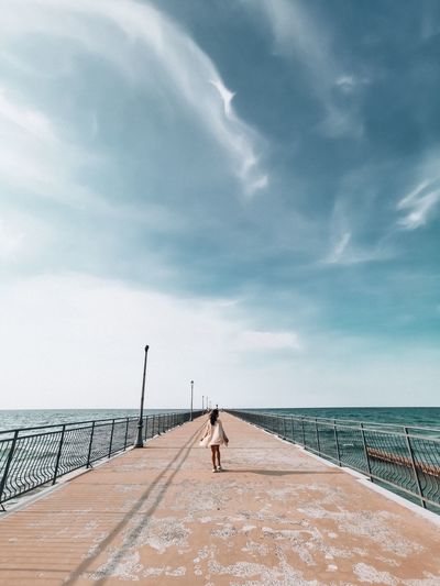Rear view of woman walking on pier over sea