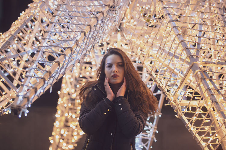 Portrait of woman standing against illuminated christmas lights at night