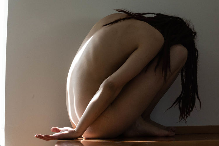 Naked woman sitting on table against wall at home