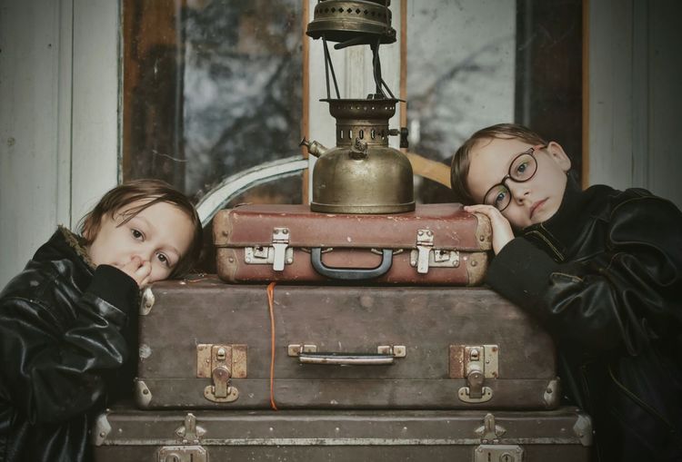 Portrait of siblings leaning on luggage outside house