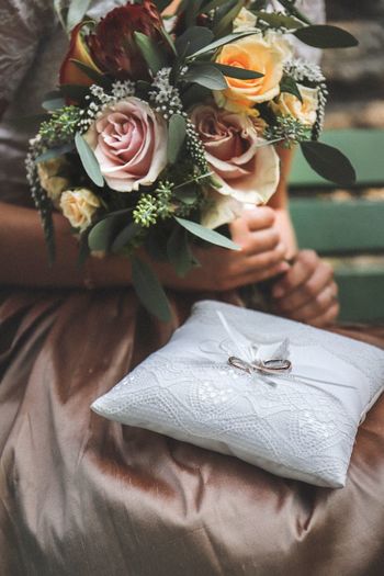 Midsection of bride holding flower bouquet with rings on pillow