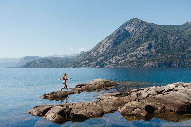 Woman in bikini walking at lakeshore against clear sky during sunny day