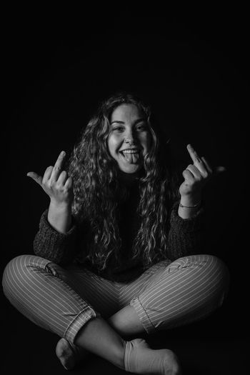 Portrait of smiling woman showing obscene gesture against black background