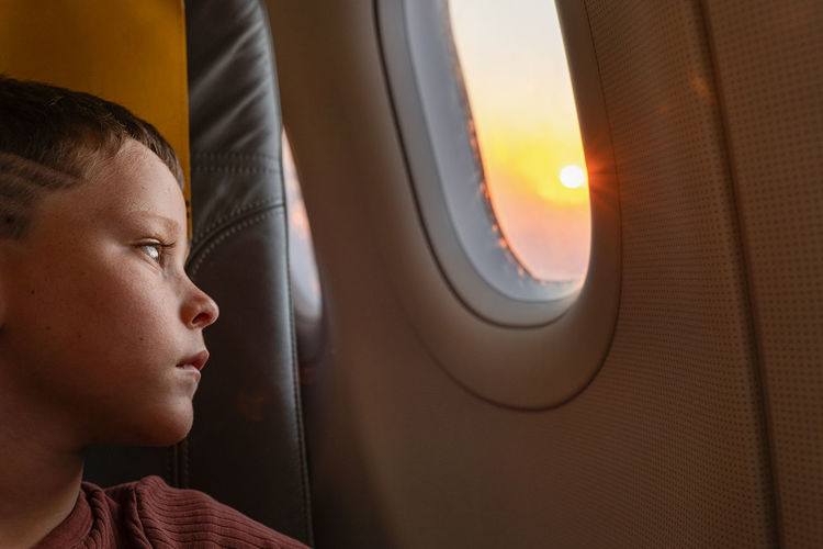 Side view of calm boy sitting on chair looking out the windows in plane