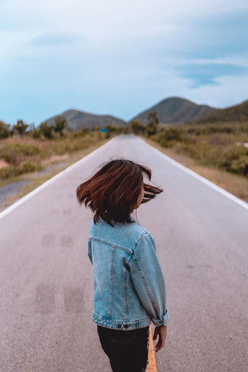 Woman with tousled hair standing on road against sky