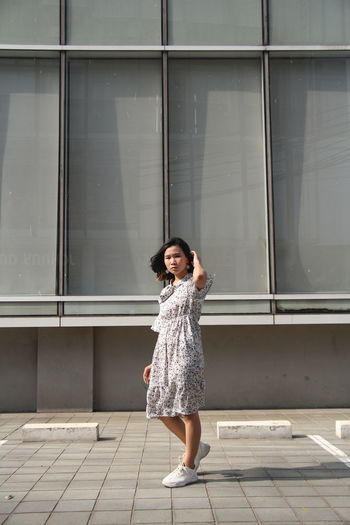 Full length portrait of woman standing against building on footpath