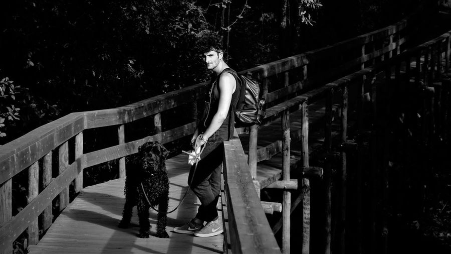 Man with black dog standing on railing against trees