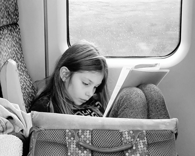 Girl reading book while sitting in train