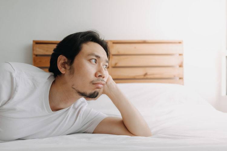 Young man looking away while sitting on bed at home