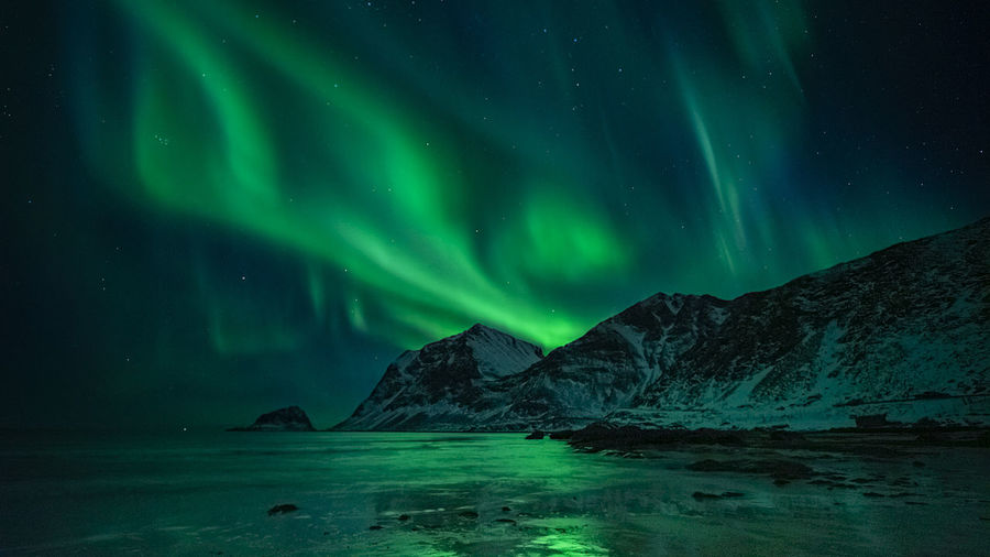 Aurora borealis over sea against sky at night
