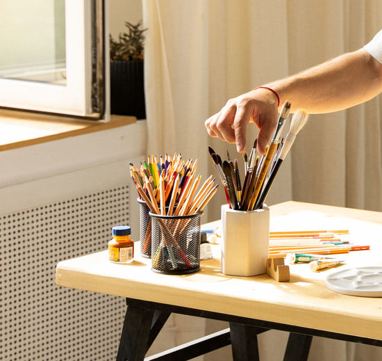 Midsection of men holding paintbrushes on table at home