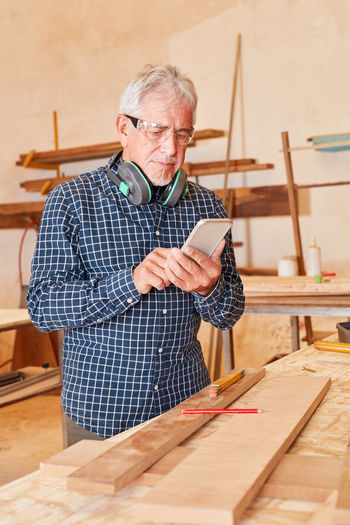 Senior carpenter using mobile phone at workshop