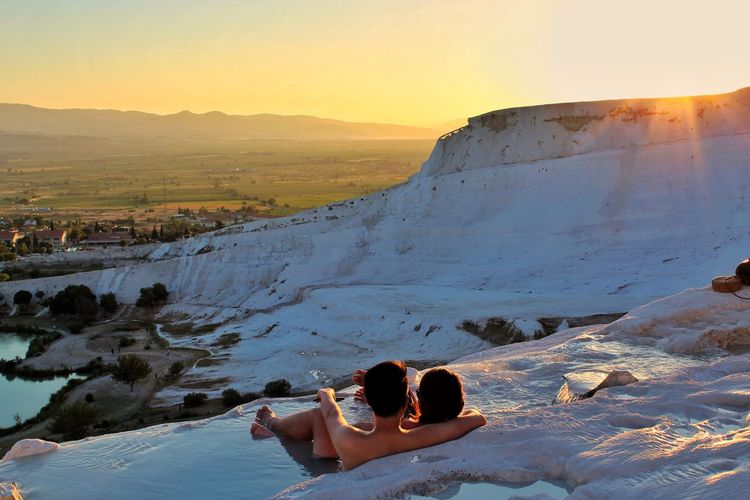 Rear view of couple lying on mountain against sky during sunset