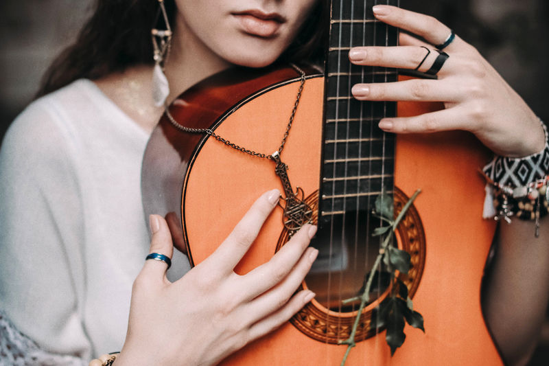 Cropped hippie girl in white blouse with boho jewelry hugging a guitar. summer spirit of freedom
