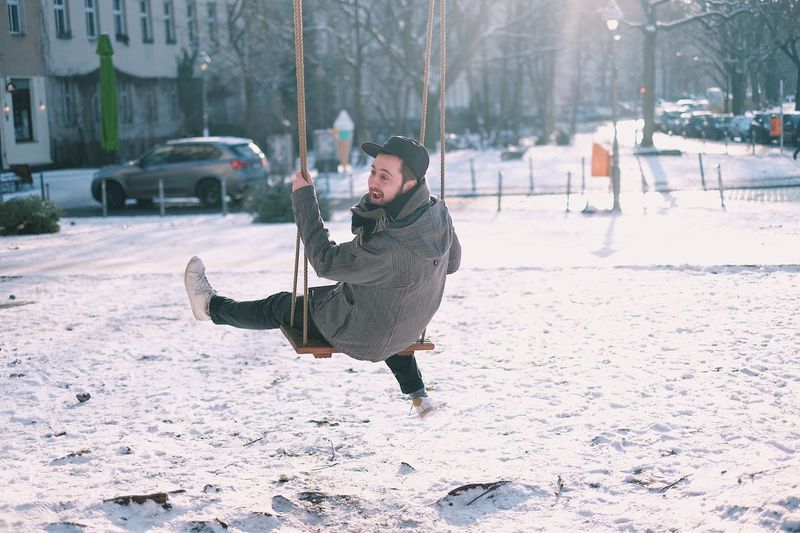 Man on swing on snow covered playground