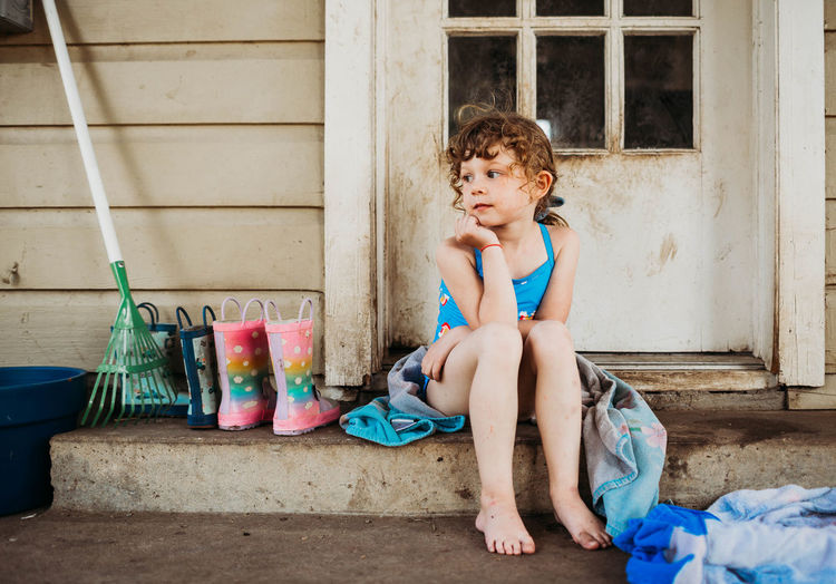 Young girl sitting on back porch wearing swim suit and towel