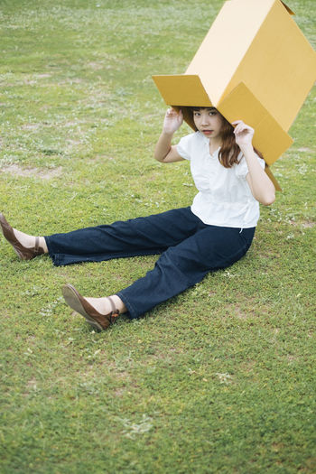 Full length portrait of woman sitting with box on grass