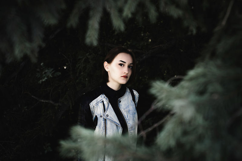 Portrait of young woman standing by trees