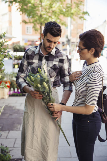 Female customer buying flowers from male owner on sidewalk