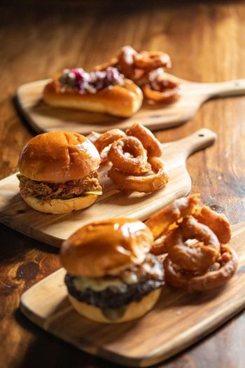 Cafe burgers and sliders with onion rings and other garnishes served on a wooden board.