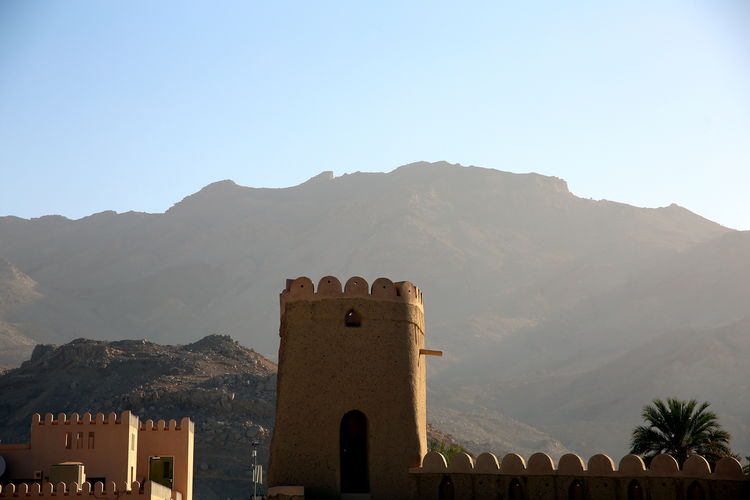 Crenellated tower with contrasting mountain backdrop illuminated by morning light, nizwa, oman