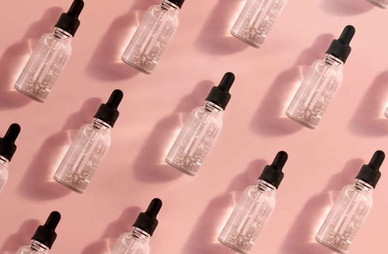 Pattern of transparent glass dropper bottle with serum on pink background. pipette with fluid acid