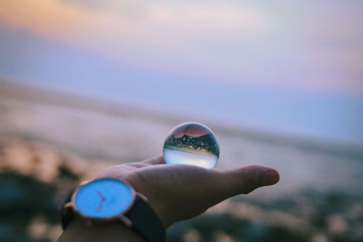Close-up of hand holding bubble against sky