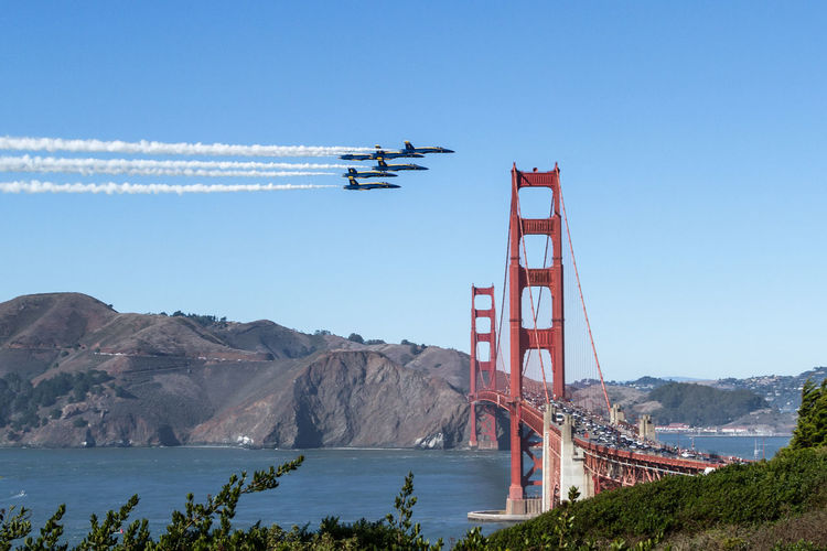 Cars moving on golden gate bridge over bay against clear blue sky during sunny day