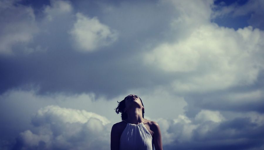 Low angle view of mid adult woman standing against cloudy sky