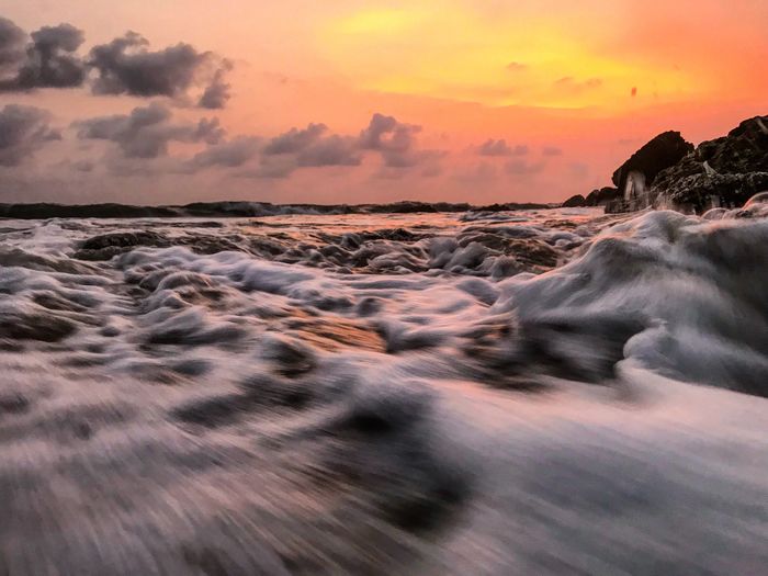 Blurred motion of waves reaching on shore at beach against orange sky